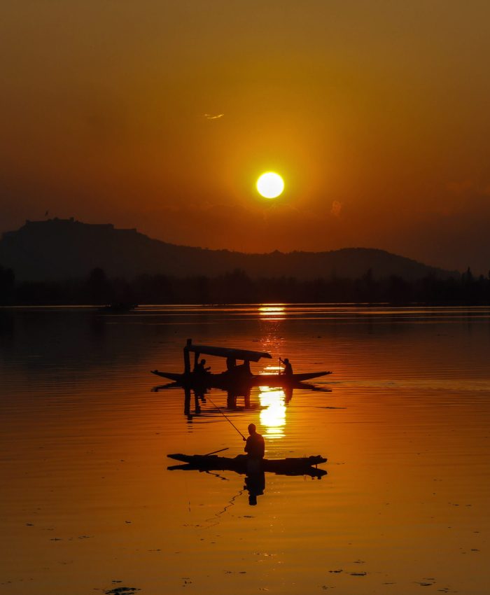 Srinagar, Sep 09 (ANI): A fisherman catching fish while people enjoy the Shikara ride as the sun sets over Dal Lake, in Srinagar on Friday. (ANI Photo)